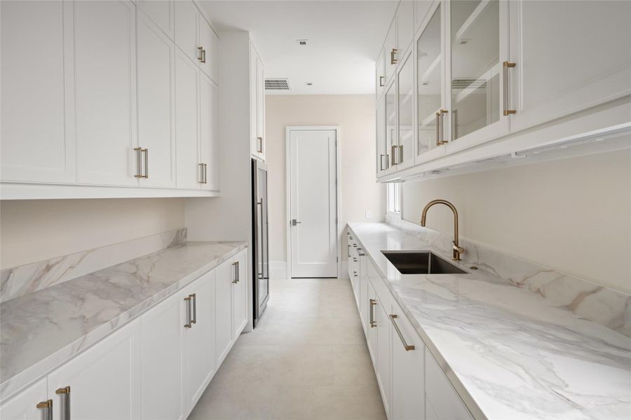 Butler’s kitchen with wine refrigeration, prep sink, dishwasher, and extensive storage, leading to a walk-in pantry beyond.