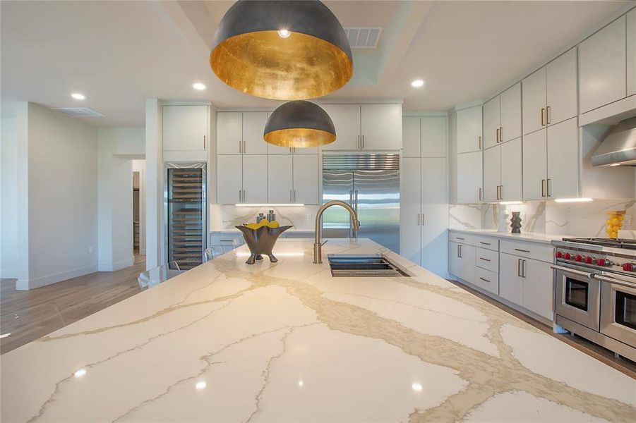 Kitchen featuring high quality appliances, sink, decorative backsplash, and light stone countertops