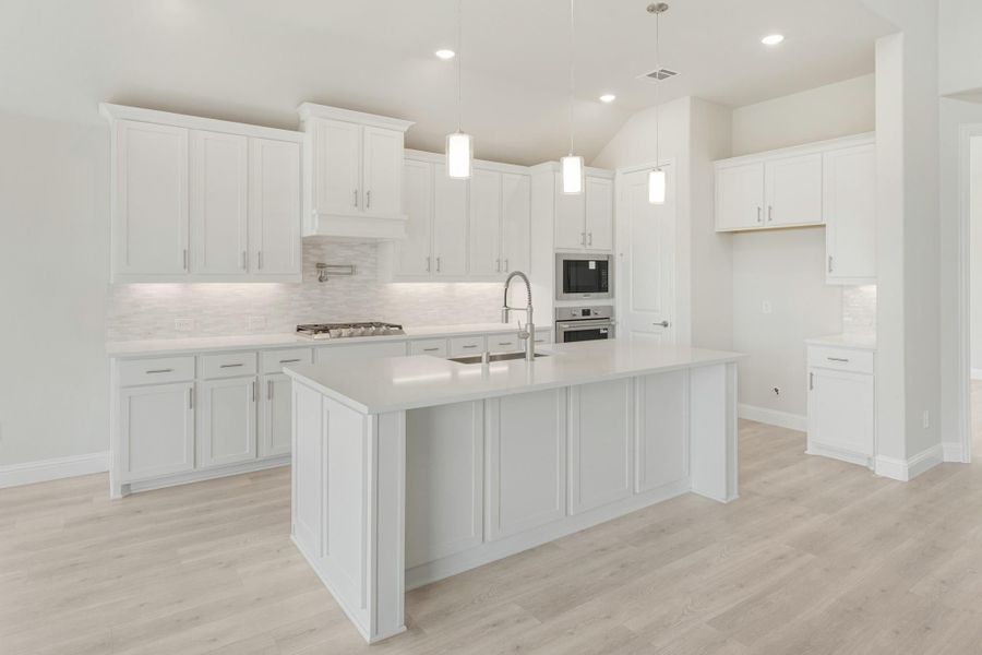 White kitchen with large center island, pendant lights, stainless steel appliances, and light wood floors