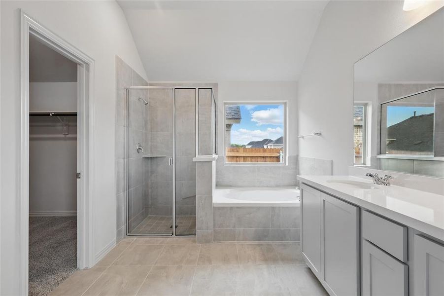Bathroom with vanity, a spacious closet, a garden tub, a shower stall, and vaulted ceiling