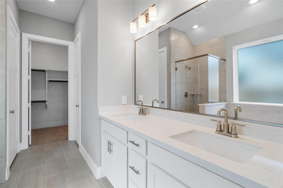 A bright and functional primary bath offering dual sinks for busy mornings, a large framed mirror, soaking tub, and a modern glass-enclosed shower, creating a serene and efficient space.