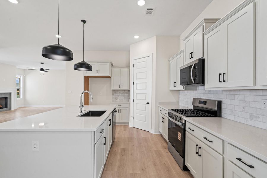 Kitchen with stainless steel appliances, a kitchen island with sink, open floor plan, a lit fireplace, and light wood-type flooring