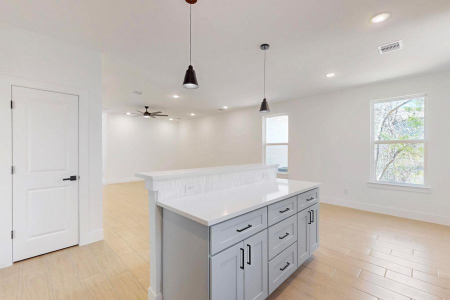 Kitchen with gray cabinets, wood tiled floors, hanging light fixtures, open floor plan, and a center island