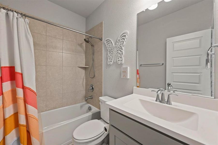 Full bath featuring shower / tub combo with curtain, vanity, and a textured wall Full bath featuring shower / tub combo with curtain, vanity, and a textured wall