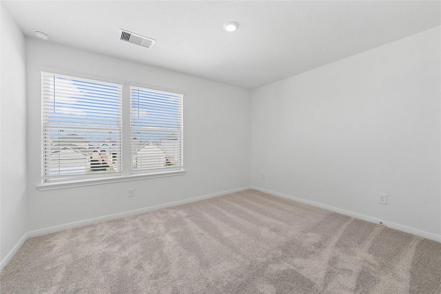 This secondary bedroom offers comfort and style with plush carpeting, neutral paint tones, recessed lighting, large windows with blinds, and a generously sized closet.