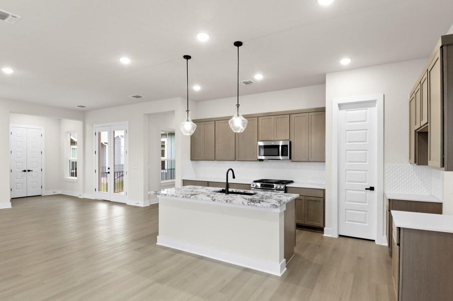 Kitchen with an island with sink, light stone countertops, pendant lighting, appliances with stainless steel finishes, and recessed lighting