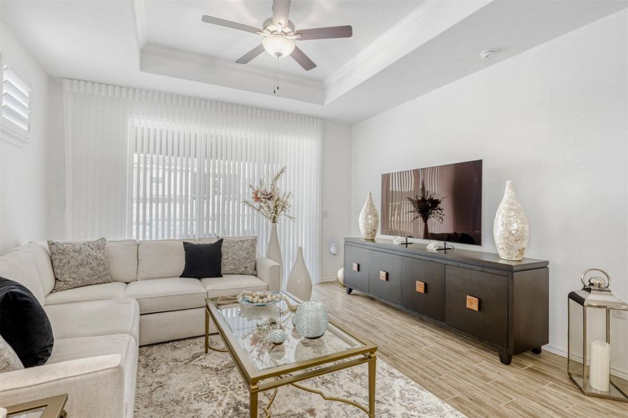 Living room with wood tiled floors, plenty of natural light, ornamental molding, ceiling fan, and a raised ceiling