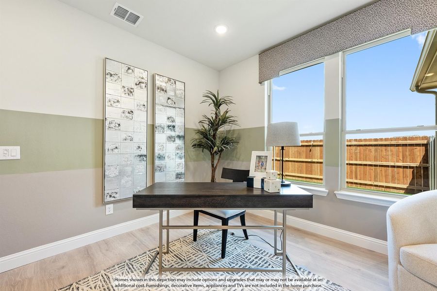 Home office with dark wood desk, light hardwood floors, and large windows overlooking backyard fence