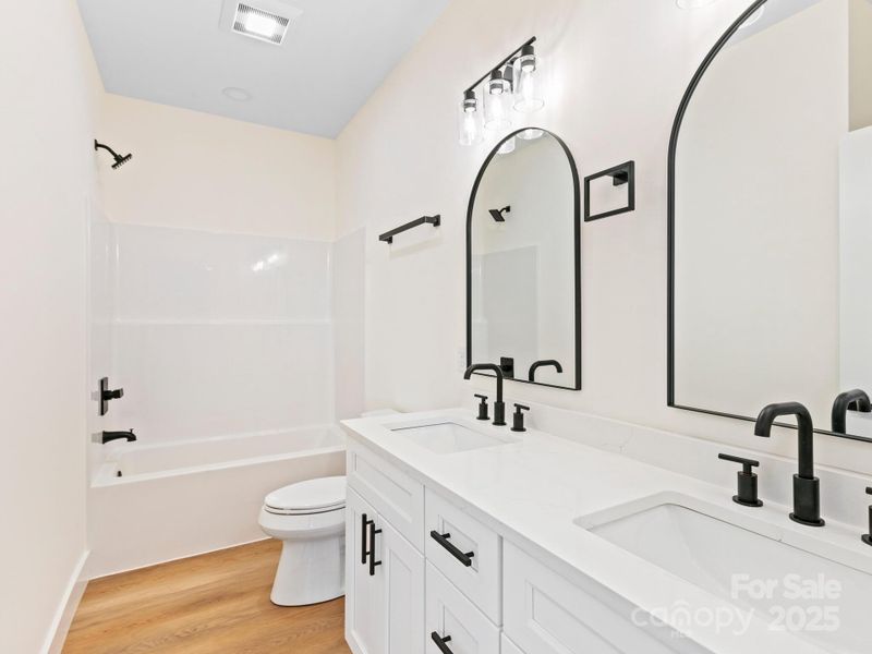 Guest hall bath also features dual sinks, quartz counters and black fixtures & hardware.