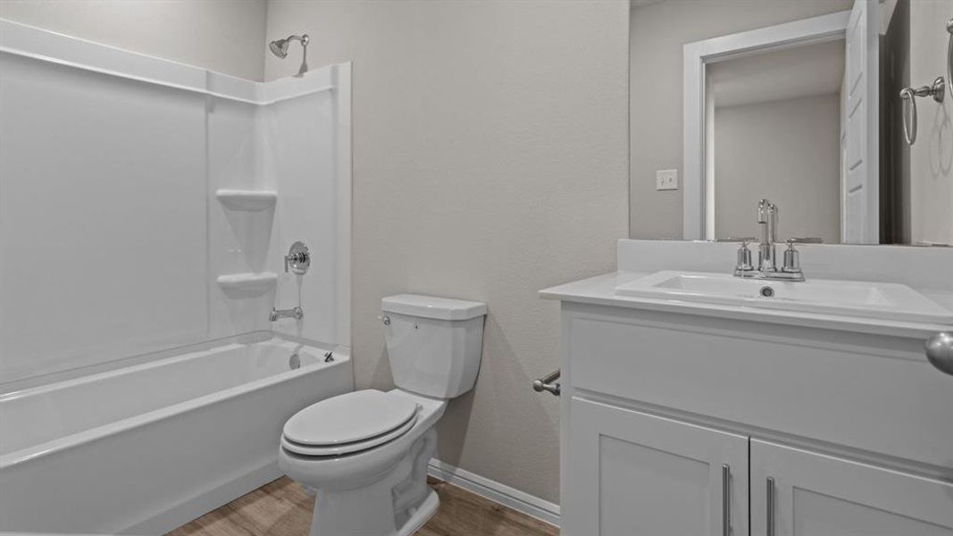 Full bathroom featuring wood finished floors, vanity, toilet, washtub / shower combination, and baseboards Full bathroom featuring wood finished floors, vanity, toilet, washtub / shower combination, and baseboards
