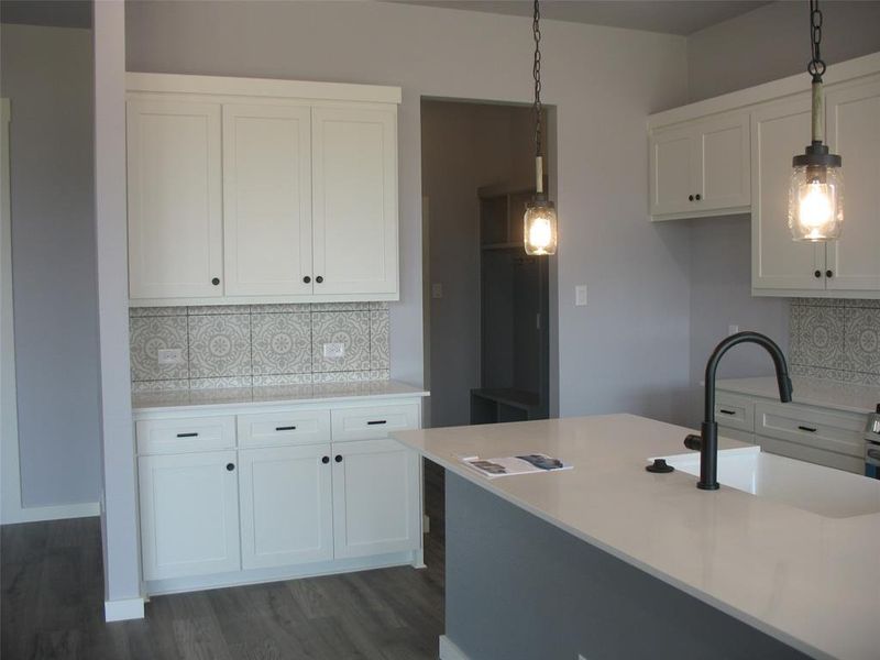 Kitchen with backsplash, pendant lighting, white cabinetry, dark wood-style floors, and light stone counters