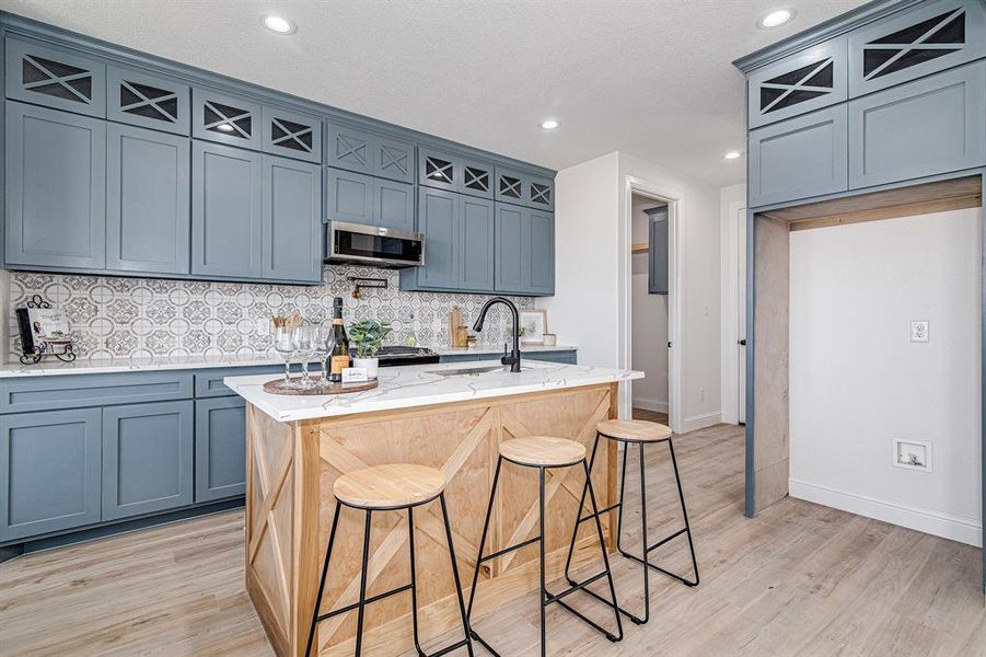 Kitchen featuring backsplash, light stone countertops, a breakfast bar, light wood finished floors, and an island with sink