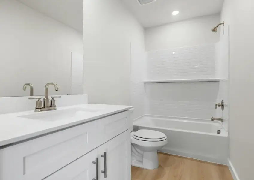 Secondary bath has a shower/tub comboe, white cabinet vanity and light luxury vinyl flooring.