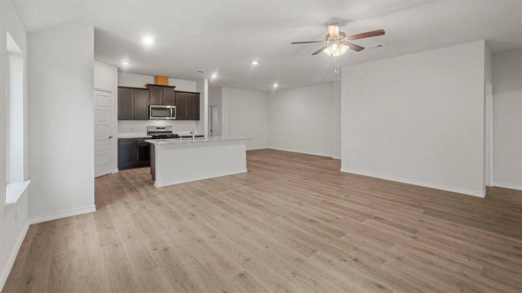 Kitchen with dark brown cabinets, light wood-style floors, an island with sink, open floor plan, and recessed lighting Kitchen with dark brown cabinets, light wood-style floors, an island with sink, open floor plan, and recessed lighting