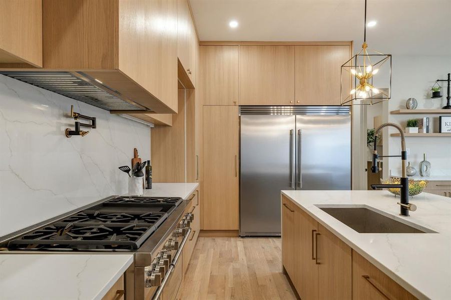 Kitchen with appliances with stainless steel finishes, premium range hood, sink, decorative light fixtures, and light stone counters