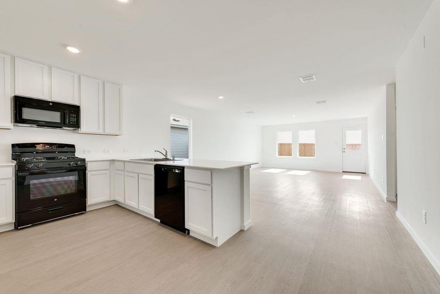 Kitchen featuring a peninsula, a sink, white cabinets, open floor plan, and black appliances