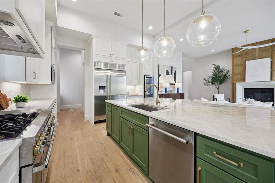 Kitchen with premium appliances, light stone counters, light wood-style floors, two tone cabinetry, and open floor plan