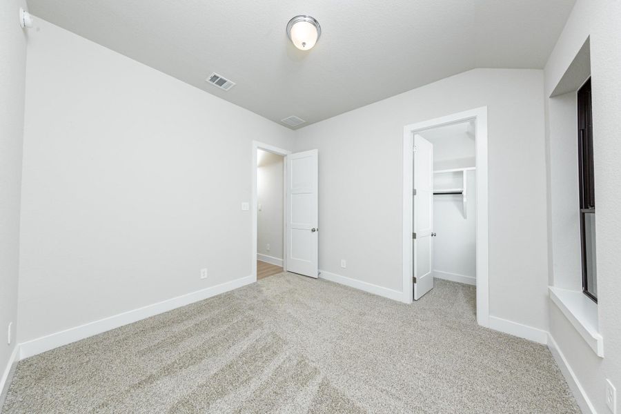 This secondary bedroom offers comfort and style with plush carpeting, neutral paint tones, recessed lighting, large windows, and a walk-in closet.