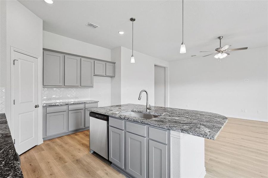 Kitchen with light hardwood / wood-style floors, sink, dark stone counters, ceiling fan, and a kitchen island with sink