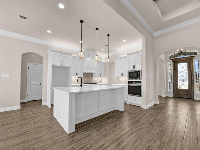 Kitchen featuring oven, white cabinets, tasteful backsplash, a kitchen island with sink, and built in microwave