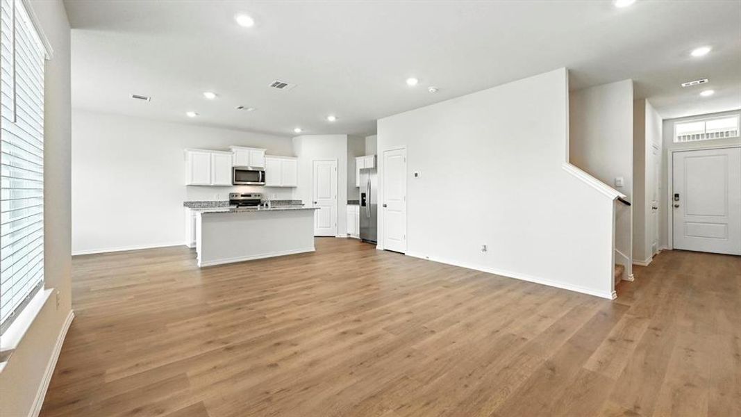 Open-concept living area featuring wood-finish flooring, recessed lighting, and a kitchen with white cabinetry