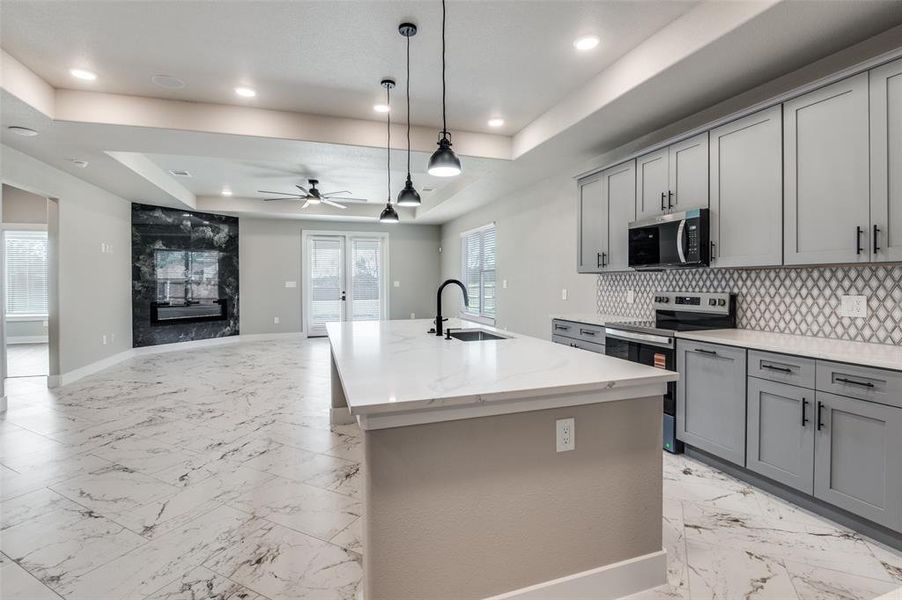 Kitchen with appliances with stainless steel finishes, a tray ceiling, pendant lighting, a kitchen island with sink, and recessed lighting