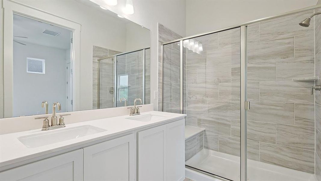 Modern bathroom featuring a dual vanity with white cabinetry and integrated sinks, brushed nickel fixtures, a full-width mirror, and a tiled walk-in shower with a glass enclosure and built-in bench