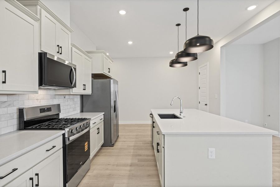Modern kitchen featuring light-toned cabinetry with black hardware, stainless steel appliances, a white subway tile backsplash, and light wood-finish flooring Modern kitchen featuring light-toned cabinetry with black hardware, stainless steel appliances, a white subway tile backsplash, and light wood-finish flooring
