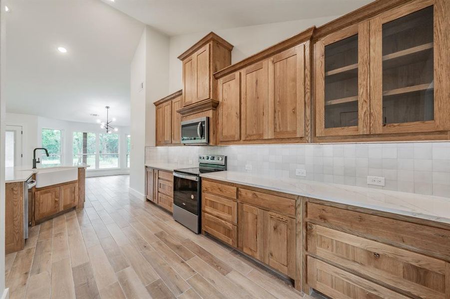 Kitchen with appliances with stainless steel finishes, a sink, brown cabinets, decorative backsplash, and a chandelier
