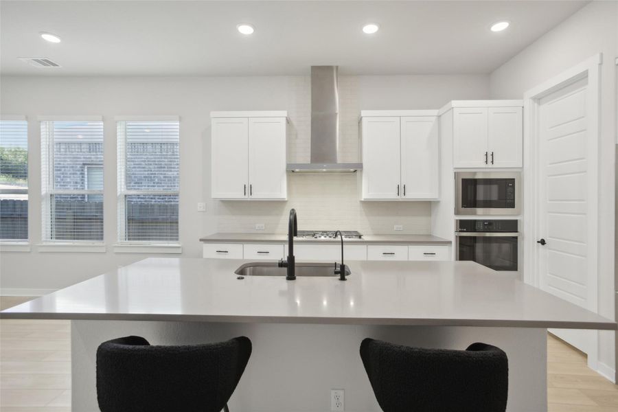 Kitchen featuring stainless steel appliances, light countertops, visible vents, a sink, and wall chimney exhaust hood