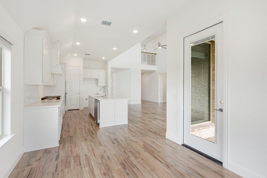 Open-concept kitchen with white cabinets, center island, and light wood floors leading to living area Open-concept kitchen with white cabinets, center island, and light wood floors leading to living area