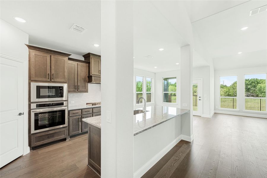 Kitchen with dark wood cabinets, stainless steel appliances, granite island, and open view to living area with hardwood floors. Kitchen with dark wood cabinets, stainless steel appliances, granite island, and open view to living area with hardwood floors.
