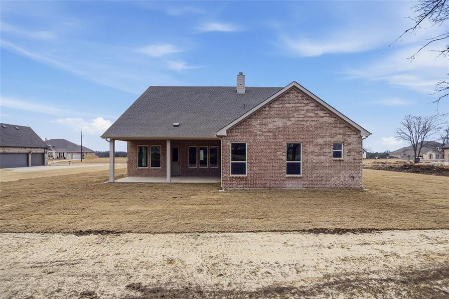 Rear view of property with a patio area, brick siding, a chimney, a yard, and a shingled roof