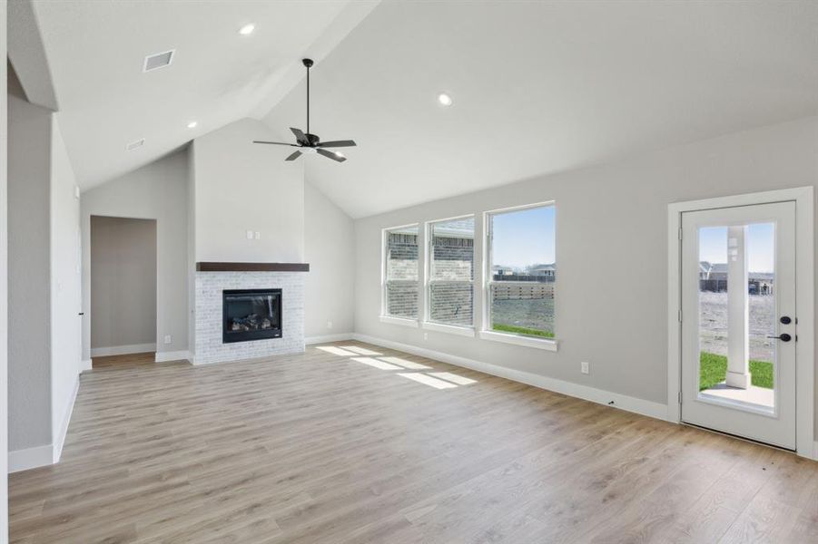 Unfurnished living room with visible vents, light wood-style flooring, a ceiling fan, a glass covered fireplace, and baseboards