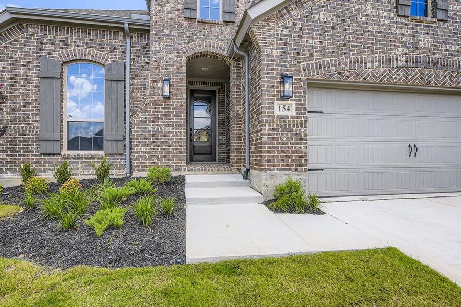 Doorway to property featuring brick siding, concrete driveway, and a garage Doorway to property featuring brick siding, concrete driveway, and a garage