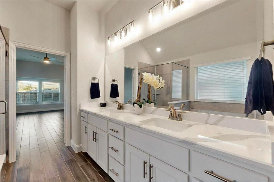 Bathroom with a ceiling fan, a stall shower, double vanity, wood finished floors, and vaulted ceiling