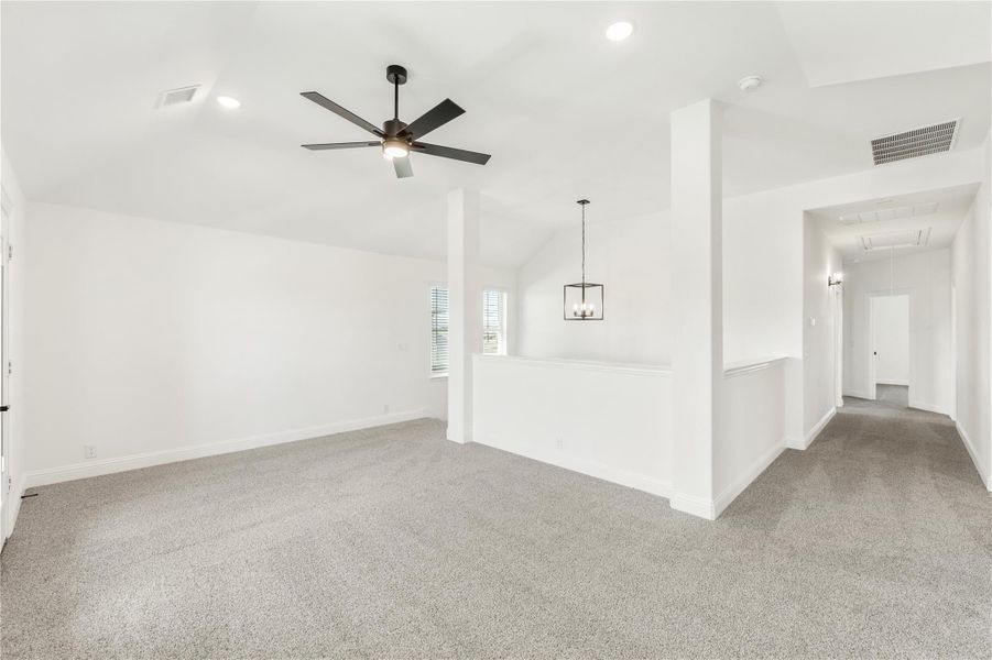 Open living area with gray carpet, ceiling fan, vaulted ceiling, and pendant light fixture Open living area with gray carpet, ceiling fan, vaulted ceiling, and pendant light fixture