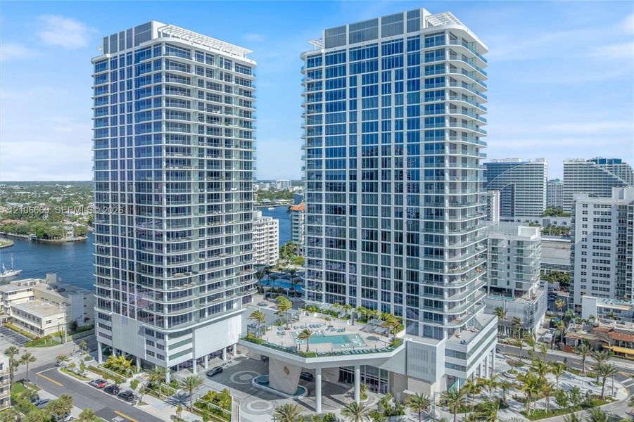 High-rise residential towers featuring floor-to-ceiling glass paneling, wrap-around balconies, an elevated podium pool deck, and structured covered entryway