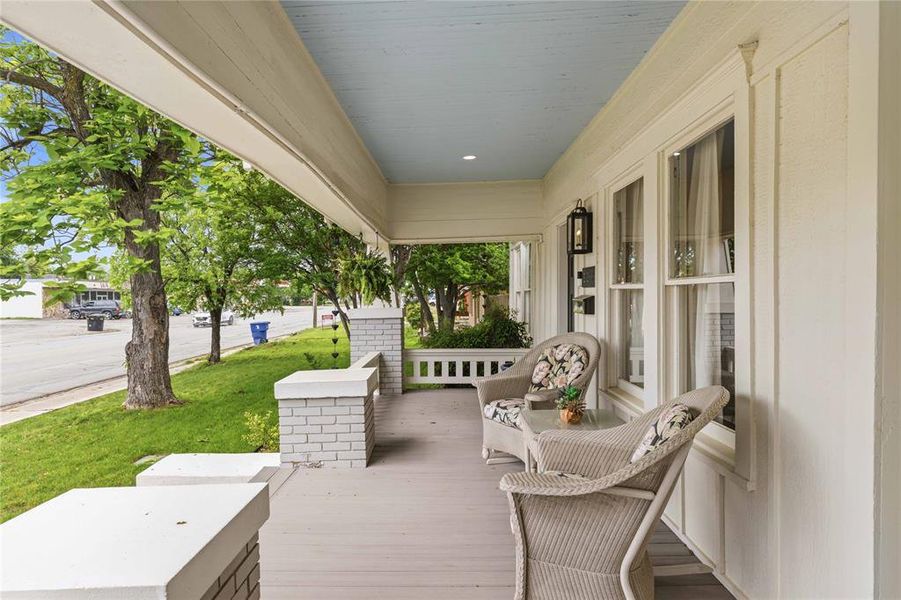 Covered front porch with light blue ceiling, white brick columns, wood-finish flooring, and exterior wall sconce