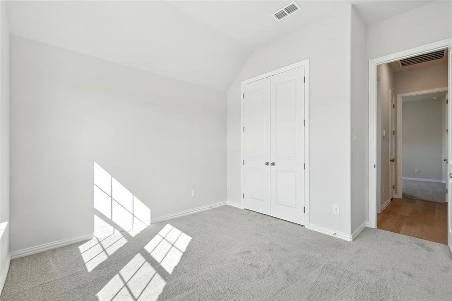 Unfurnished bedroom with light carpet, a closet, and lofted ceiling Unfurnished bedroom with light carpet, a closet, and lofted ceiling