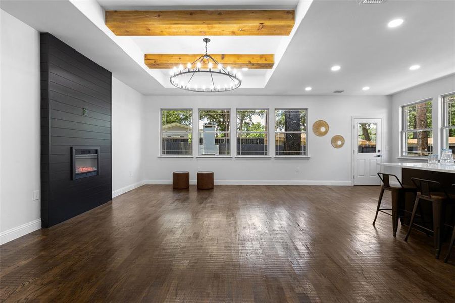 Unfurnished living room with beamed ceiling, a chandelier, dark wood-style floors, a large fireplace, and healthy amount of natural light