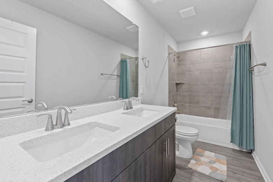 Full bathroom featuring double vanity, shower / tub combo, toilet, and a sink Full bathroom featuring double vanity, shower / tub combo, toilet, and a sink