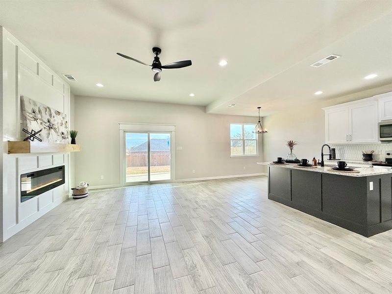 Kitchen with hanging light fixtures, light wood-type flooring, ceiling fan, light stone countertops, and white cabinets