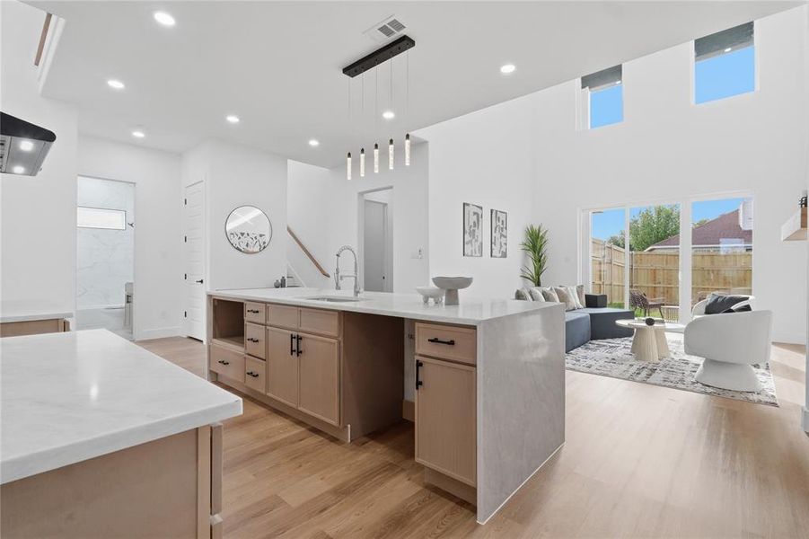 Kitchen with light wood finish cabinetry, a kitchen island with sink, light wood-style floors, open floor plan, and pendant lighting