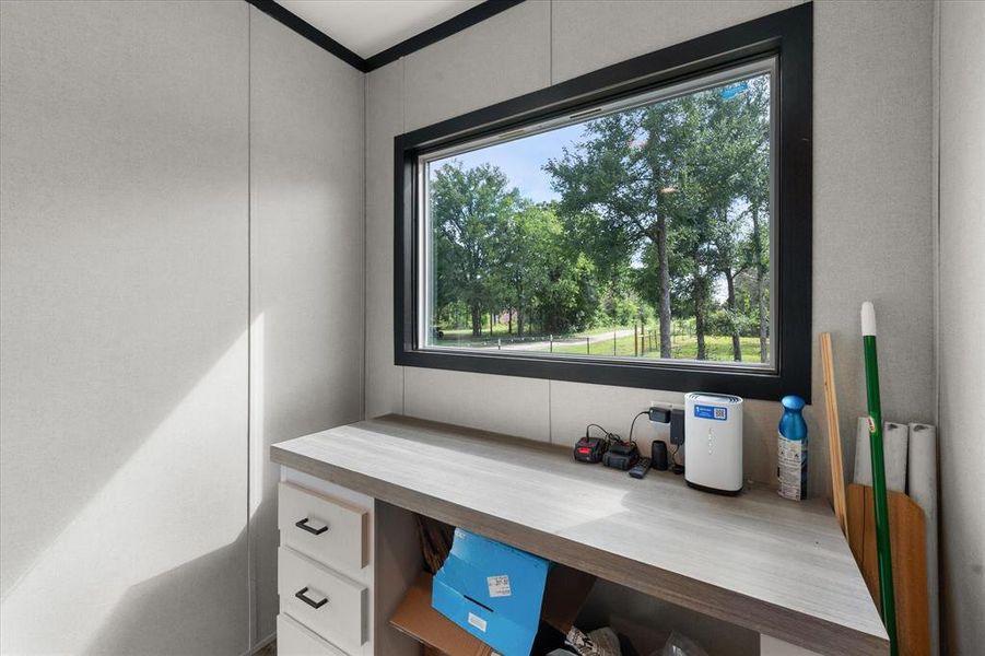 Built-in desk featuring a light wood-finish countertop, white cabinetry with dark hardware, and a large horizontal window Built-in desk featuring a light wood-finish countertop, white cabinetry with dark hardware, and a large horizontal window