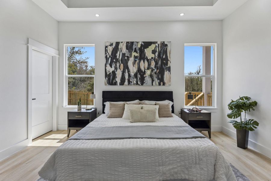 Sunlight streams through tall windows highlighting the wood floors and high tray ceiling.