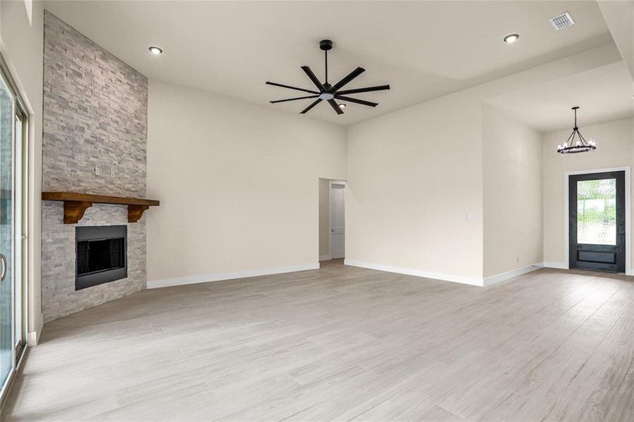 Unfurnished living room with a chandelier, a fireplace, light wood-style flooring, ceiling fan, and recessed lighting Unfurnished living room with a chandelier, a fireplace, light wood-style flooring, ceiling fan, and recessed lighting