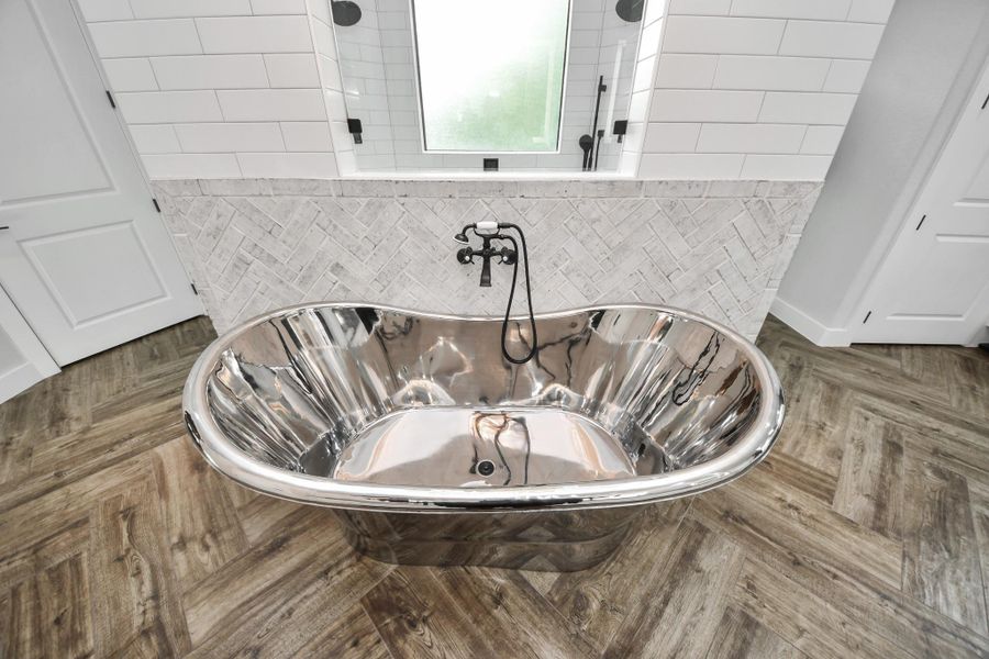 Luxurious bathroom featuring a sleek, freestanding chrome bathtub with elegant herringbone tile accents and warm wood flooring.