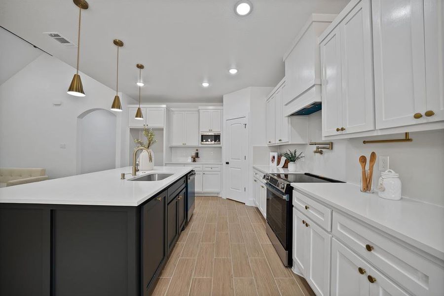 Kitchen featuring white cabinetry, stainless steel appliances, light countertops, lofted ceiling, and a kitchen island with sink