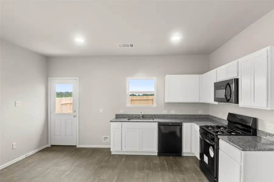 Kitchen with black appliances, light wood-style flooring, white cabinets, and recessed lighting